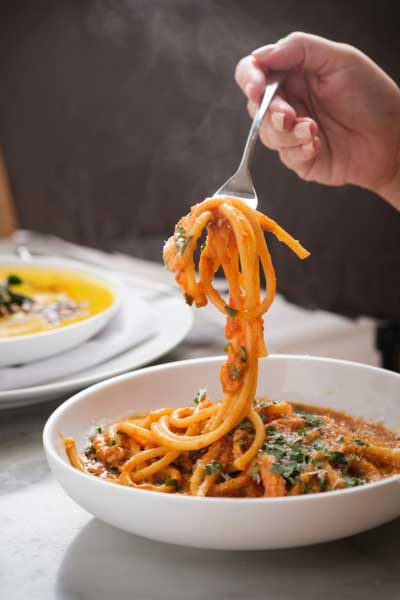 Hand pulling up on a bowl of pasta with fork